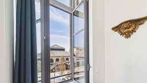 Una habitación con un ventanal grande, vista a un edificio con un letrero que dice "LES MAILLES" y un marco dorado decorativo en la pared.
