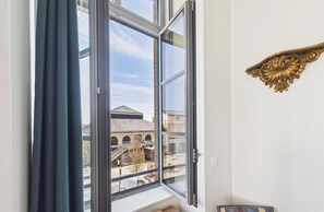 A room with a large window, a view of a building with a sign reading "LES MAILLES," and a decorative gold frame on the wall. - -LE BOUDOIR- ÉLÉGANT T2 CONCARNEAU HYPERCENTRE (Concarneau)