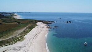 Vista aérea de una playa con un camino despejado a lo largo de la orilla, un barco anclado cerca del agua y una costa lejana con vegetación.
