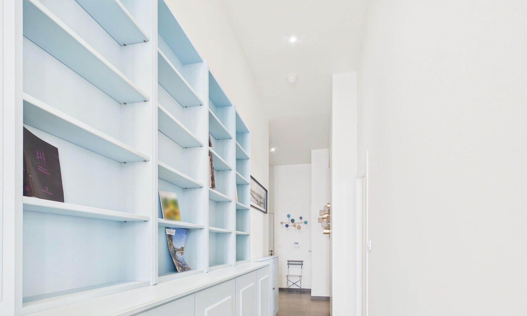 A hallway with light blue shelving units, a white door, and a wall-mounted art piece.