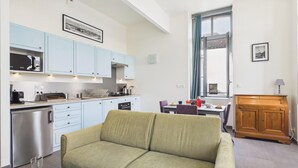 Una cocina compacta con armarios azul claro, un refrigerador de acero inoxidable y un comedor con mesa y sillas.