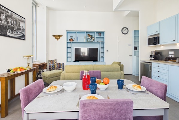 A modern living room with a dining table set for two, a sofa, and a TV mounted on the wall.