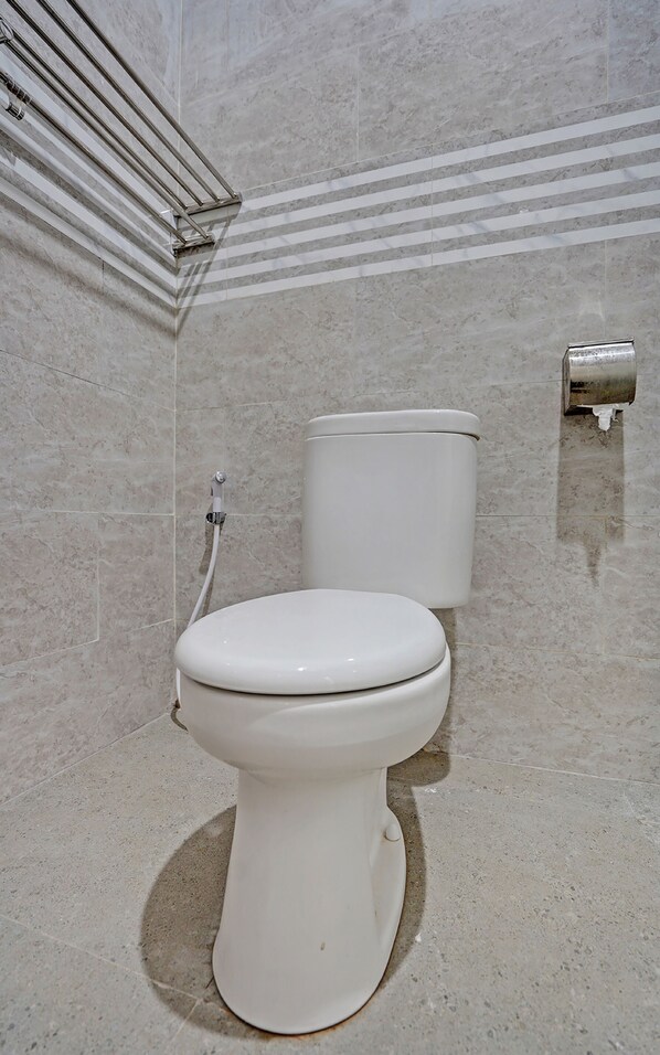 A bathroom with a white toilet, a marble-tiled wall, and a metal towel rack. - OYO 91997 Edhotel Smk Models Syariah (Kesilir)
