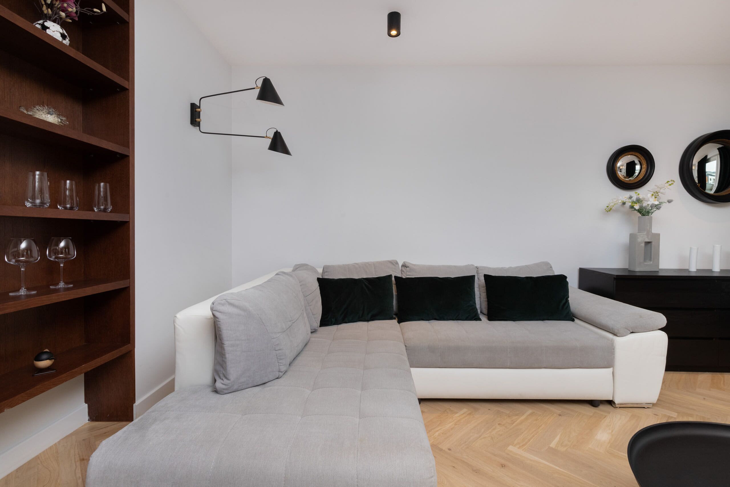 Una sala de estar moderna con un sofá modular, una estantería de madera y una pequeña mesita con un florero.