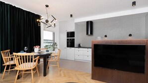 A modern kitchen with white cabinets, a black range hood, and a large flat-screen TV mounted on the wall.