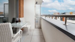 A balcony with a glass table, wicker chairs, and a clear glass door leading to a shower.