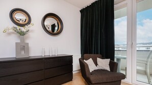 A modern room with a dark brown sofa, a dresser, two round mirrors, and a window with a view of buildings.