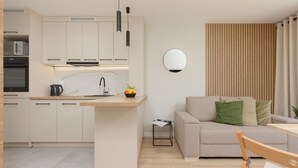 Una cocina moderna con una isla central, un comedor con mesa y sillas, y una sala de estar con sofá y cojines.