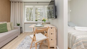 Un espacio habitable compacto con sofá, un escritorio de madera con silla, cama y televisor montado en la pared.