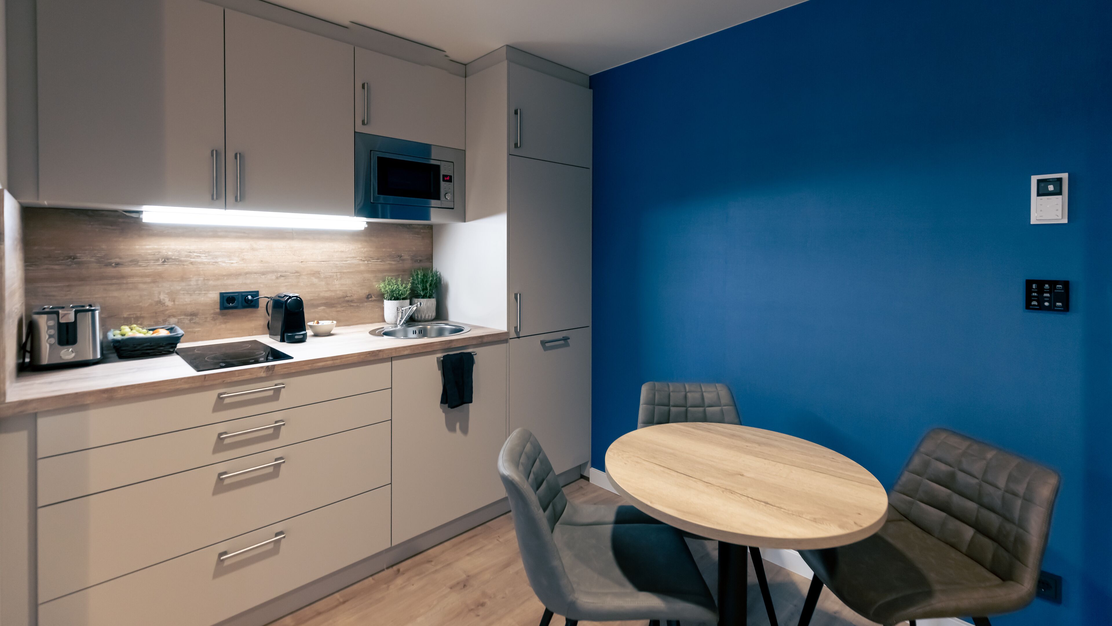 A modern kitchen with a wooden countertop, a microwave, a toaster, and a sink. There are two chairs and a small round table.