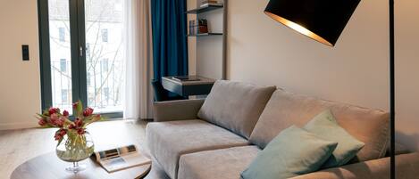 A modern living room with a sofa, a coffee table with a vase of flowers, a bookshelf, and a floor lamp.
