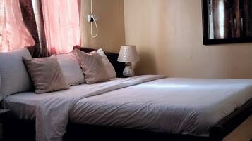 Una cama bien hecha con almohadas, una lámpara de noche y un enchufe en la pared.