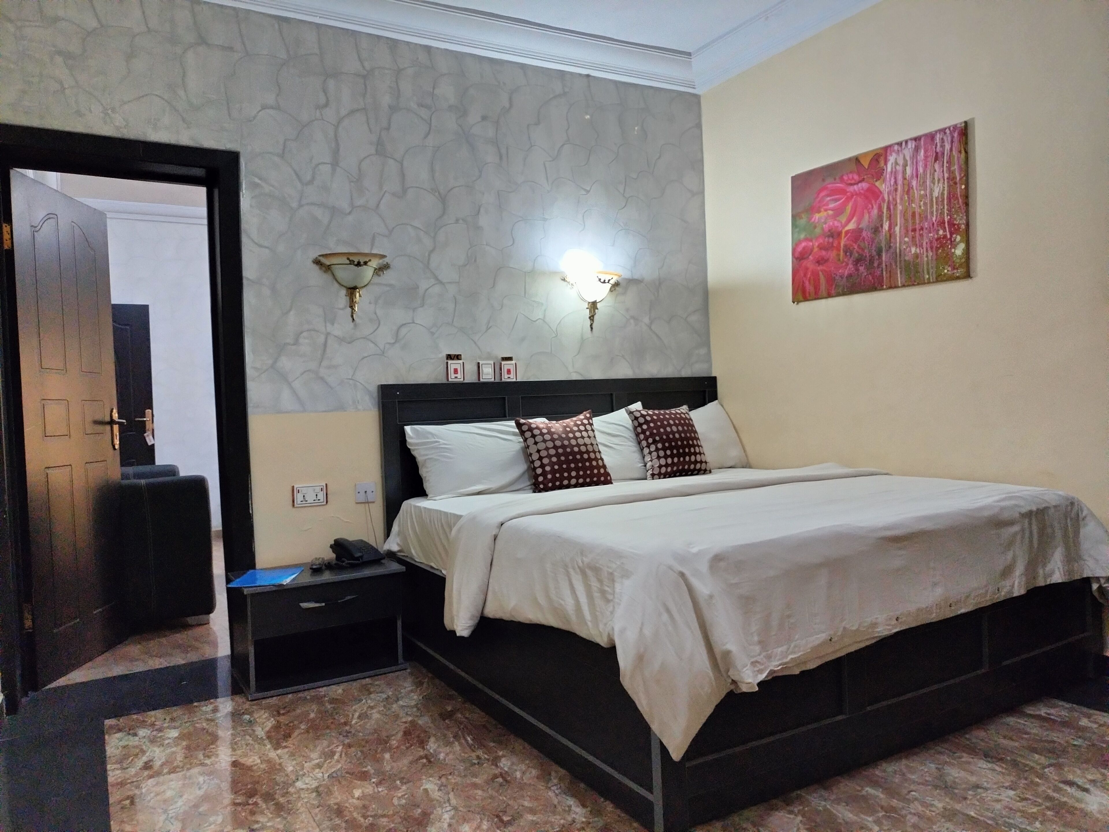 A bedroom with a bed, a nightstand, a wall-mounted light, and a painting.