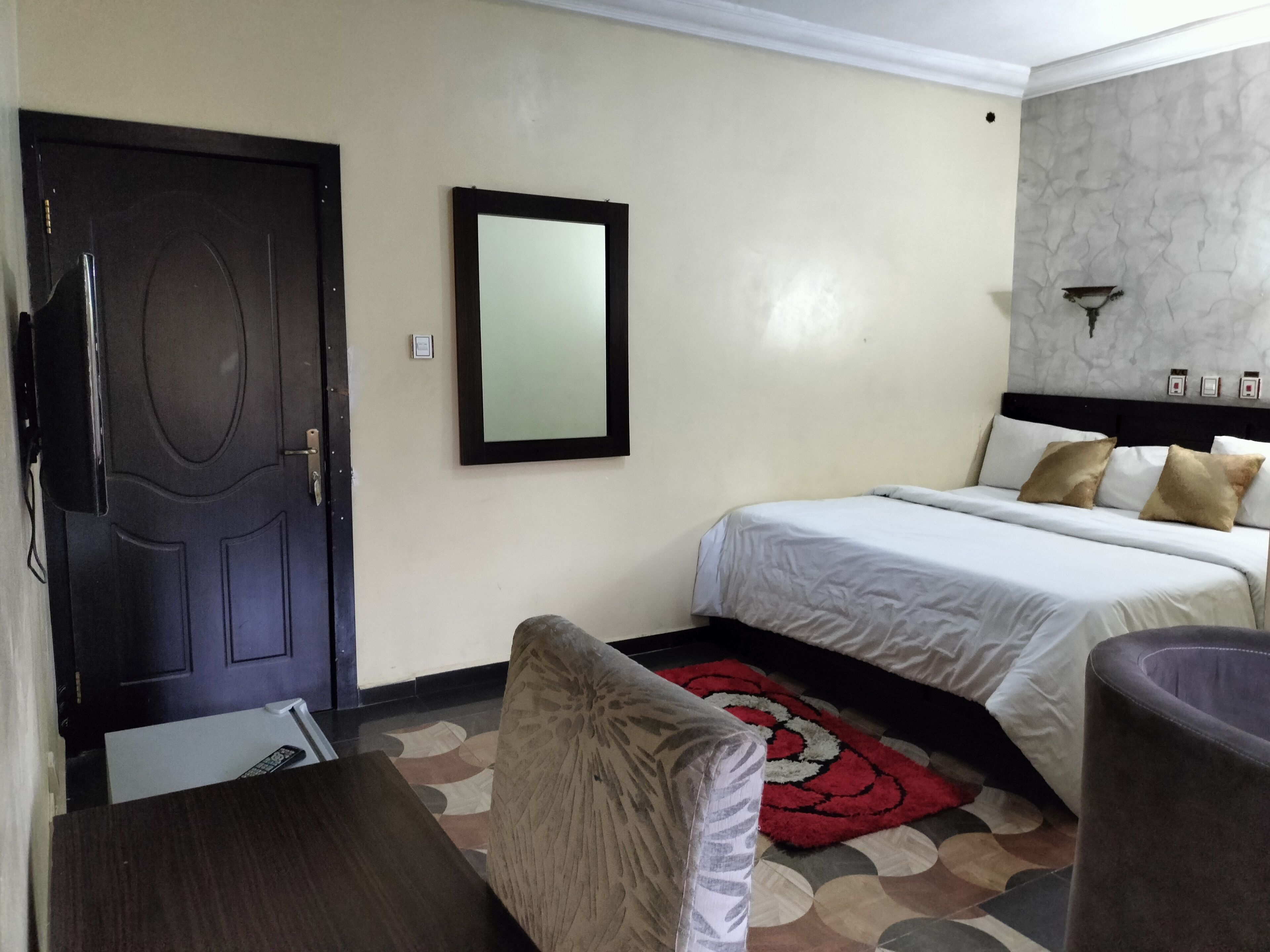 Habitación de hotel con dos camas, un escritorio, una silla, una puerta, un espejo y una alfombra estampada.