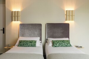 Two twin beds with headboards, a bedside table with a cup and book, and wall-mounted lighting.