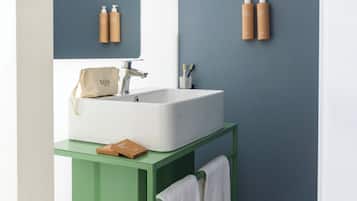 Un baño con un lavamanos blanco, tocador verde, toallero y un par de pantuflas en el suelo.