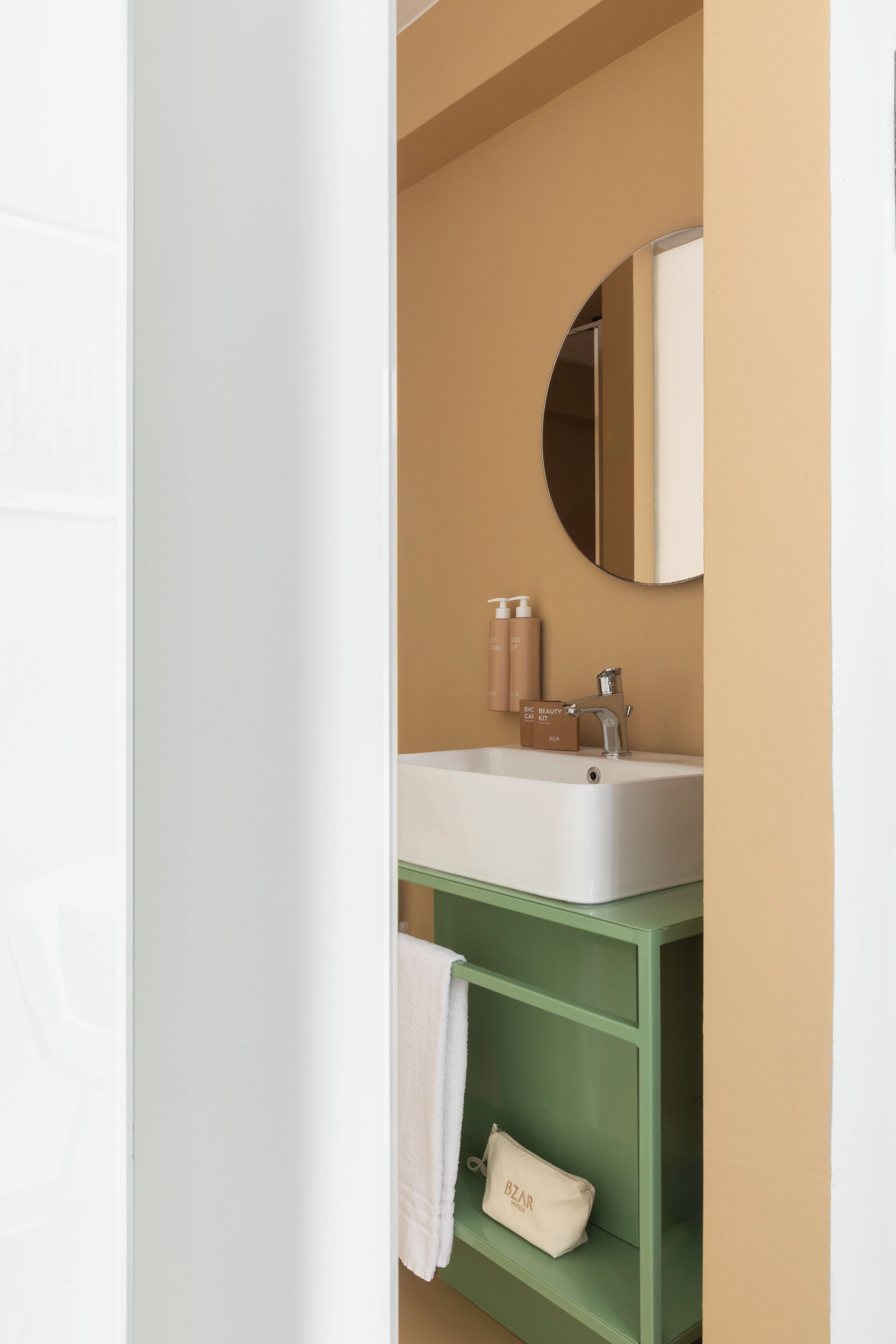 A bathroom with a white sink, green vanity, a round mirror, and a towel rack.