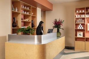 A reception desk with a woman standing behind it, surrounded by shelves with various items.