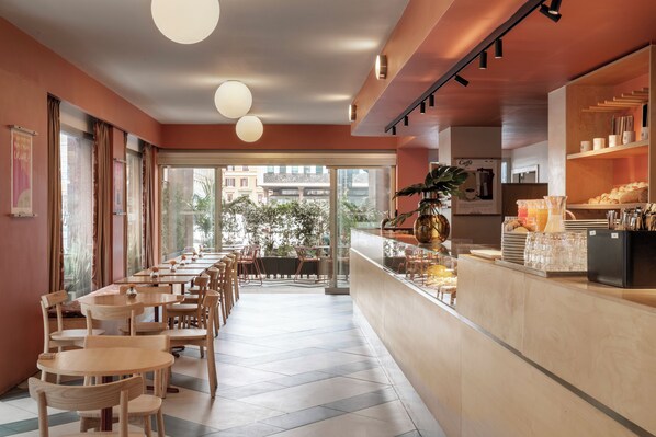 Un café avec des tables et des chaises en bois, un comptoir où sont exposées des pâtisseries, et une vue sur la rue.