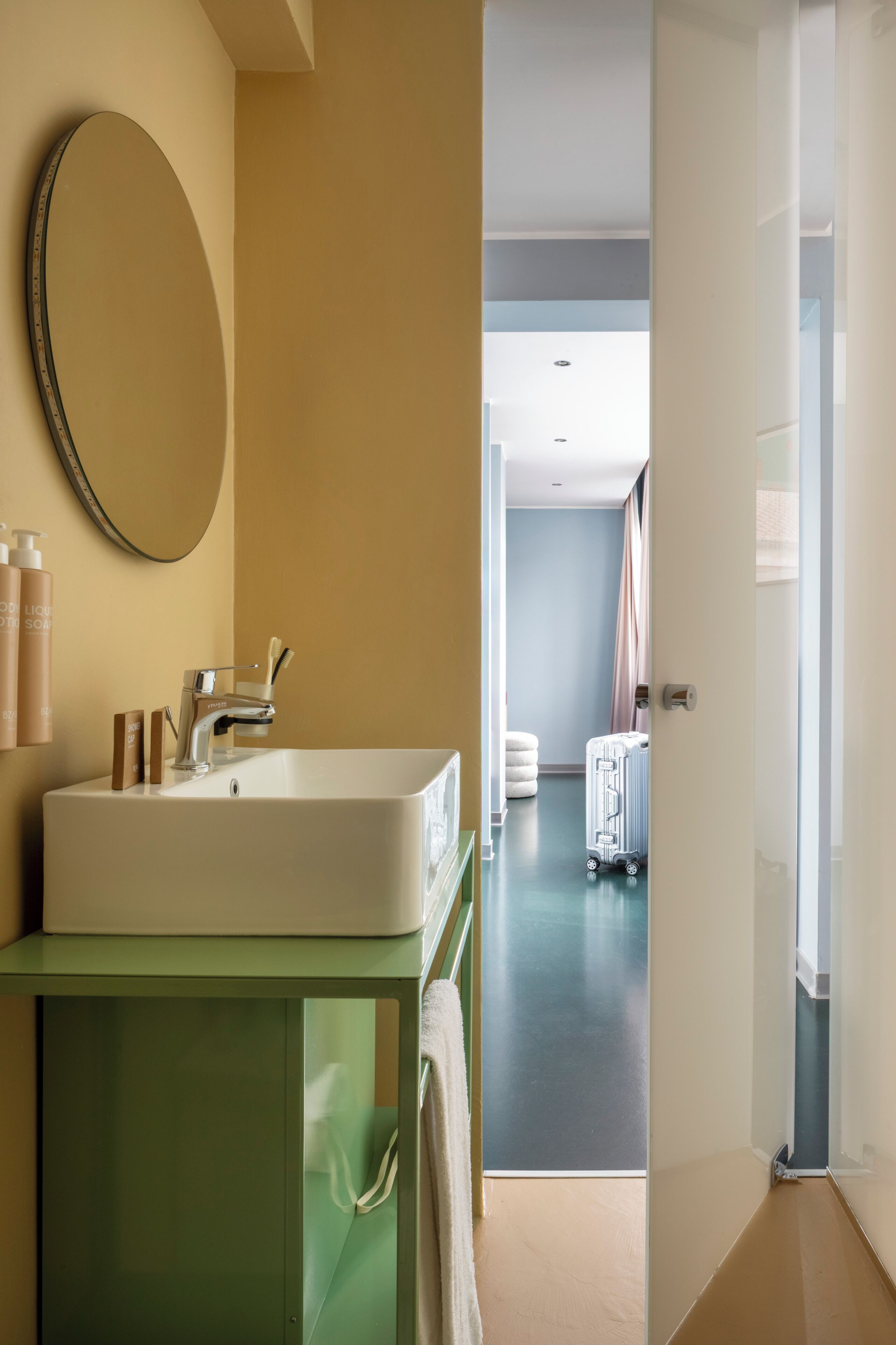 Un baño con un espejo grande, un lavabo y artículos de aseo sobre un mueble verde.