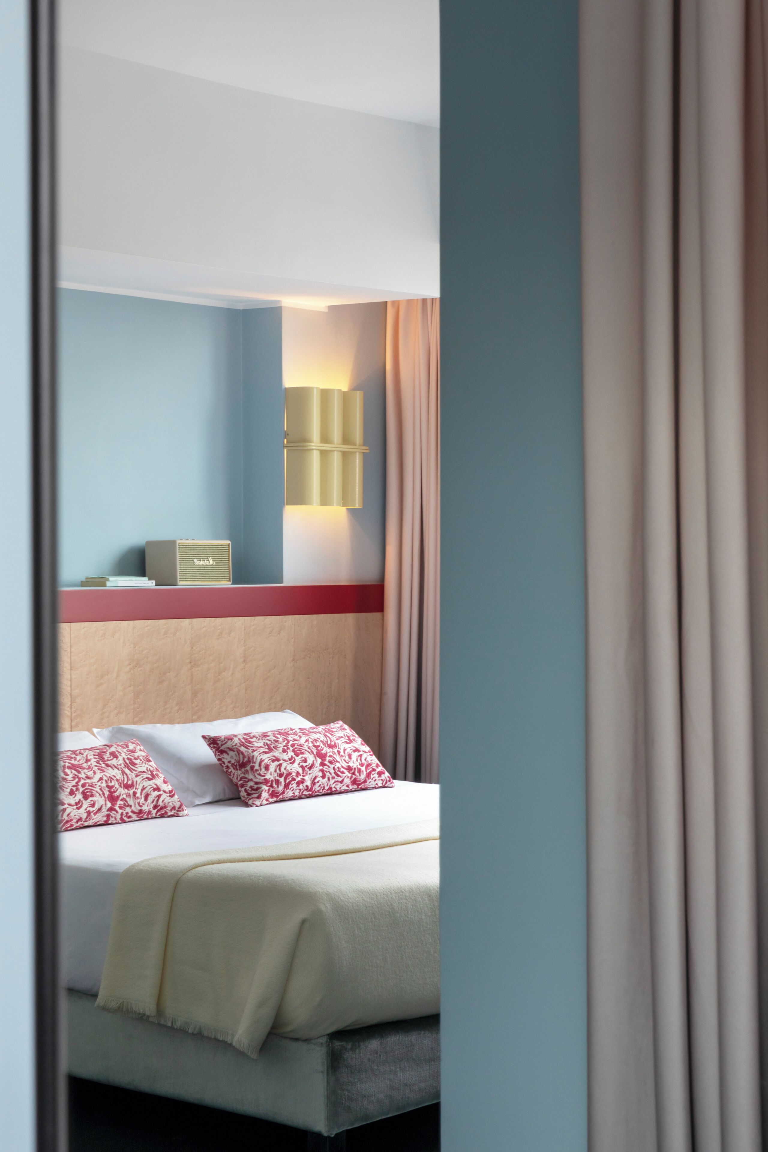 A hotel room with a bed, a bedside table, a lamp, and a window with curtains.