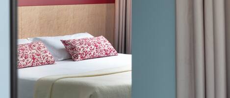 A hotel room with a bed, a bedside table, a lamp, and a window with curtains.