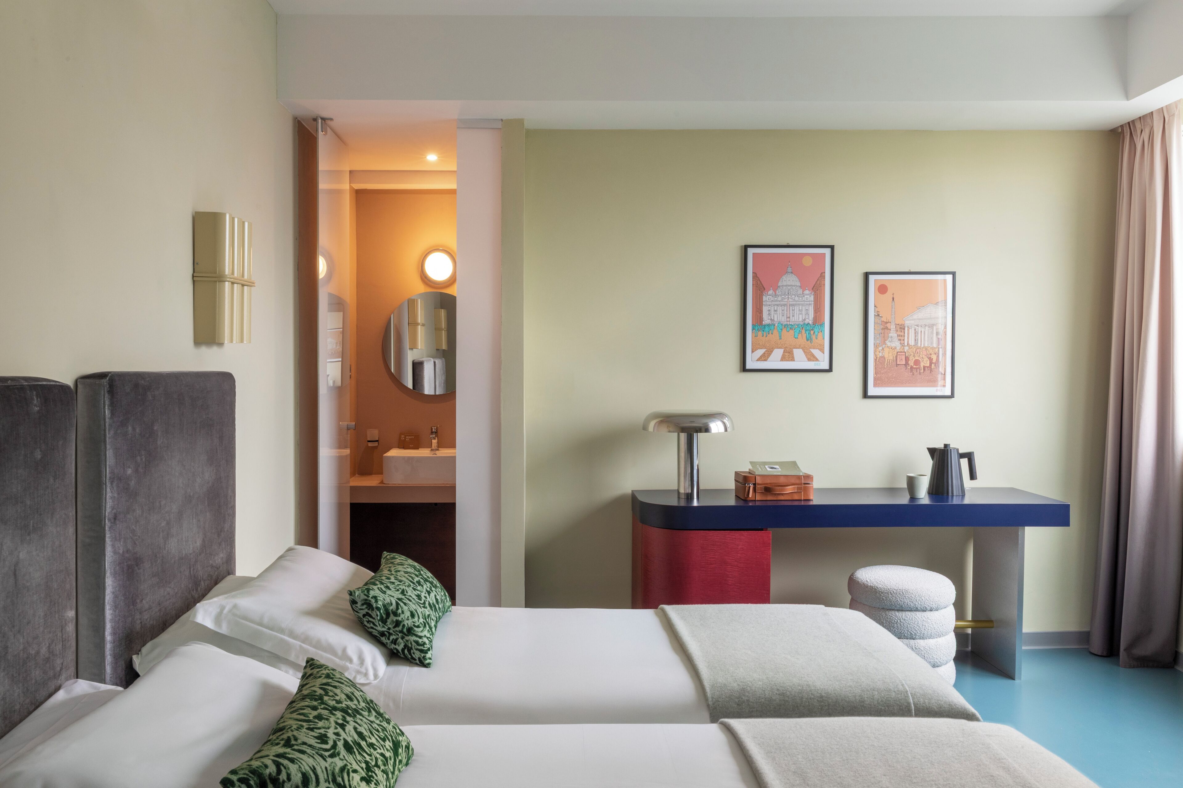 Une chambre d’hôtel avec deux lits, un bureau, un miroir et deux tableaux encadrés au mur.
