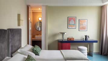Une chambre d’hôtel avec deux lits, un bureau, un miroir et deux tableaux encadrés au mur.