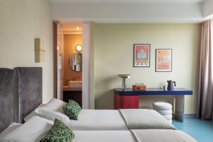 Una camera d'albergo con due letti, una scrivania, uno specchio e due quadri appesi al muro.