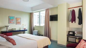 Una habitación de hotel con cama, escritorio, televisión, armario y ventana.