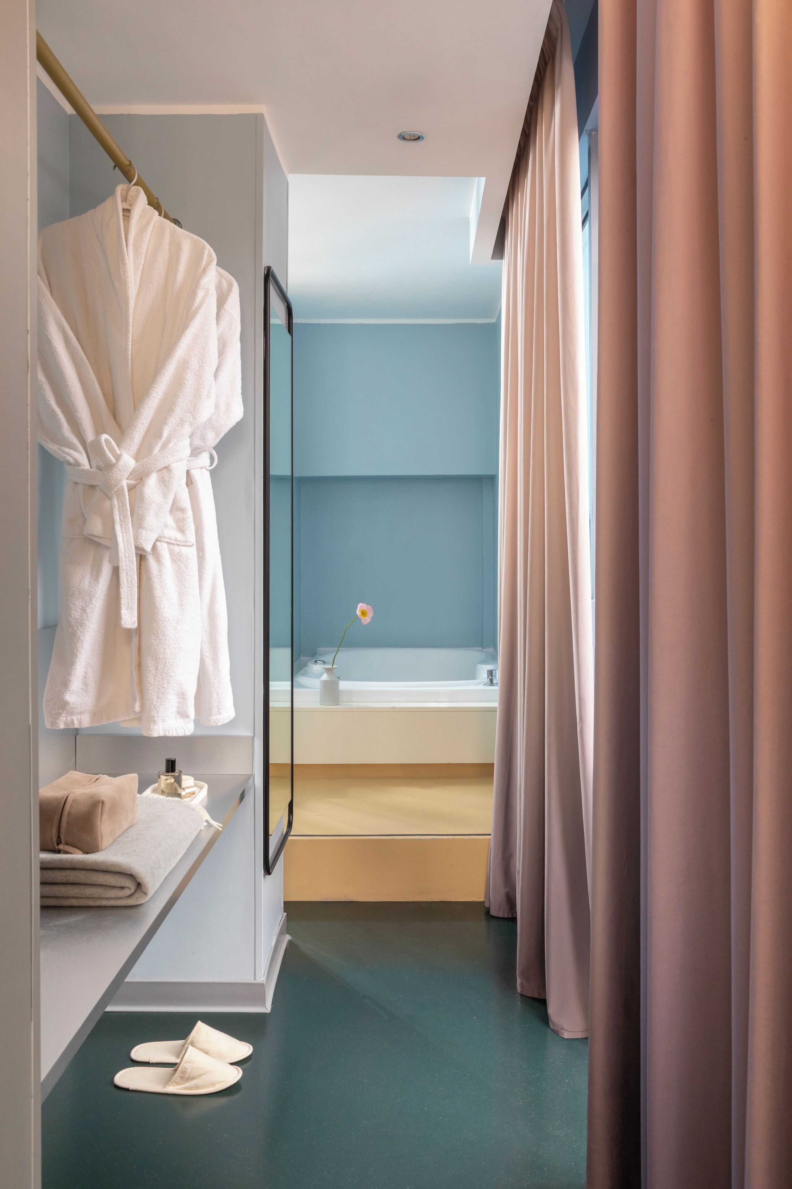 A bathroom with a bathtub, a glass shower enclosure, a robe hanging on a rack, and a towel on a shelf.