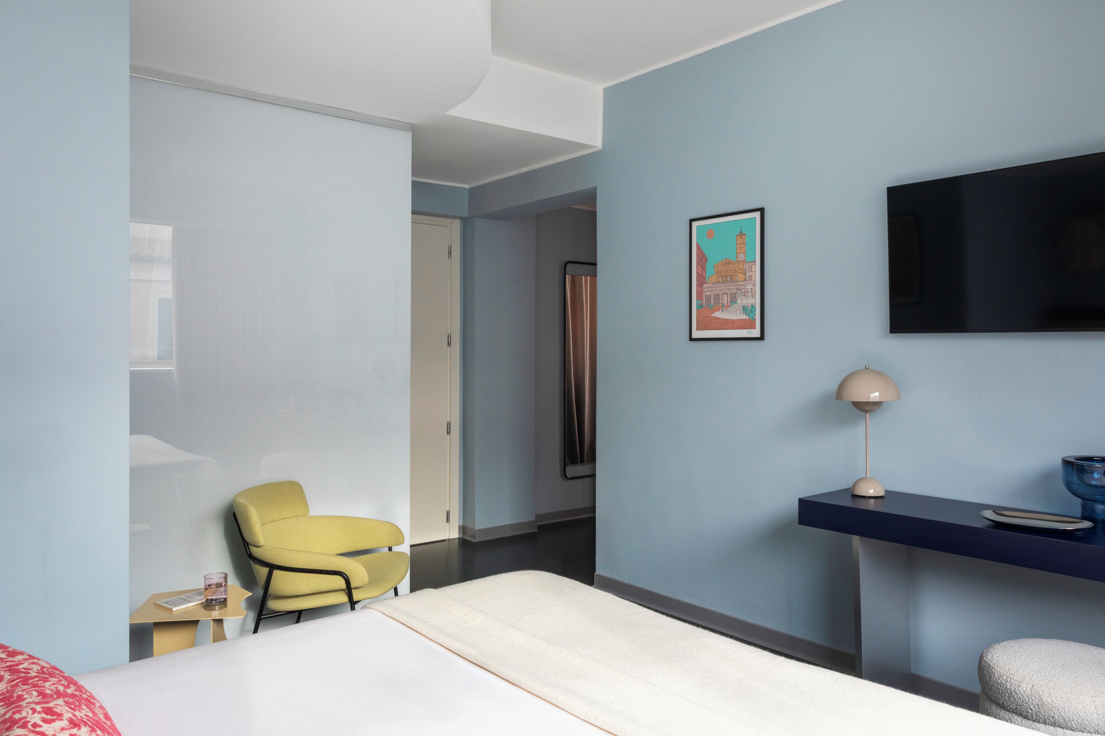 A modern hotel room with a bed, a desk, a chair, a TV, and a framed picture on the wall.