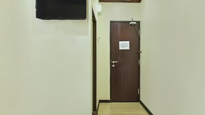 A narrow hallway with a wooden floor, a closed door with a sign, and a bed with white bedding. - EXPRESS O 91176 Hotel Puri Gandaria (Parepare)