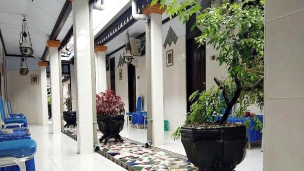A corridor with blue chairs, black planters, and a tiled floor. - EXPRESS O 91176 Hotel Puri Gandaria (Parepare)