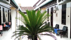 A courtyard with a central palm tree, seating areas, and a tiled floor. - EXPRESS O 91176 Hotel Puri Gandaria (Parepare)