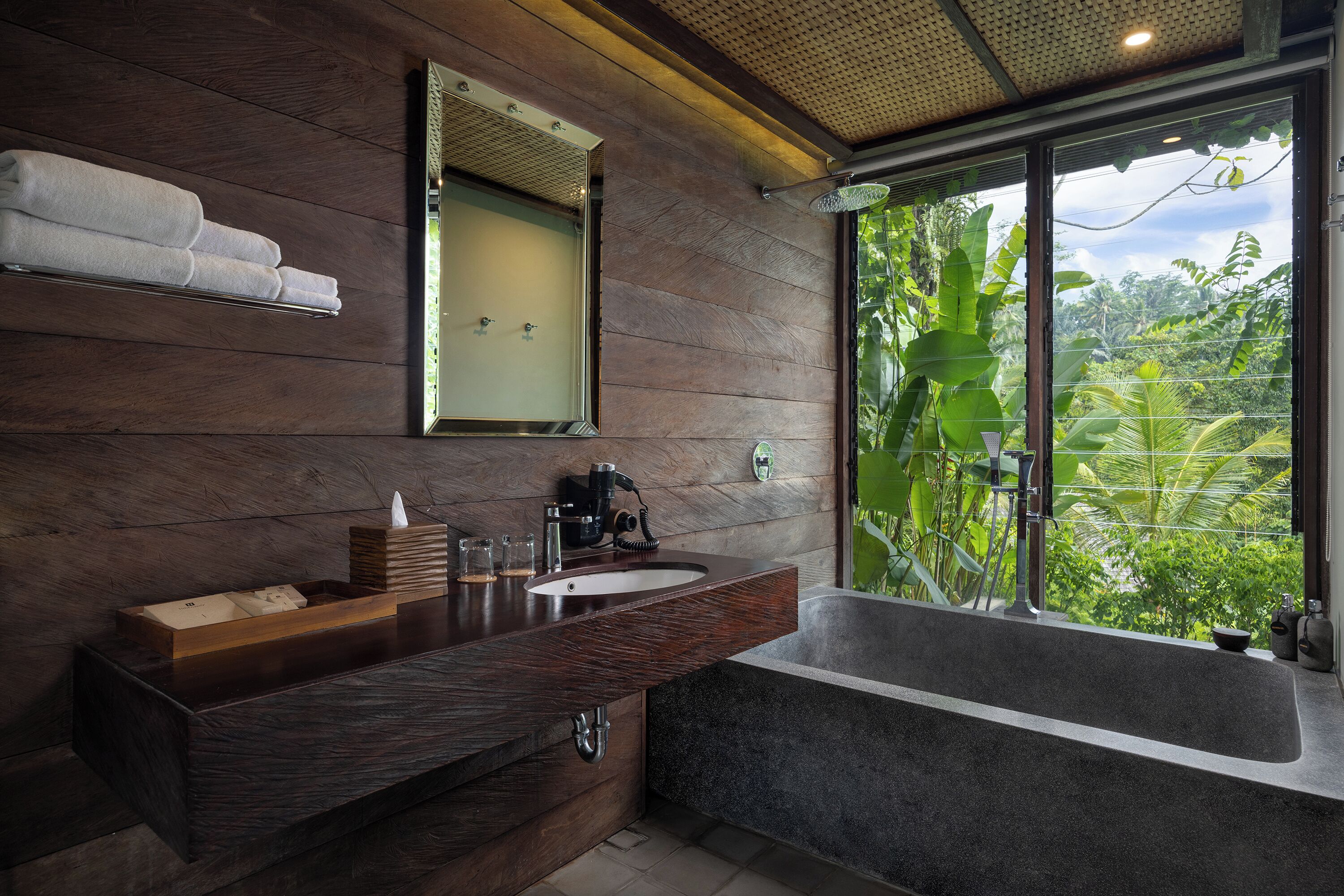 A modern bathroom with a wooden vanity, a large mirror, and a bathtub.