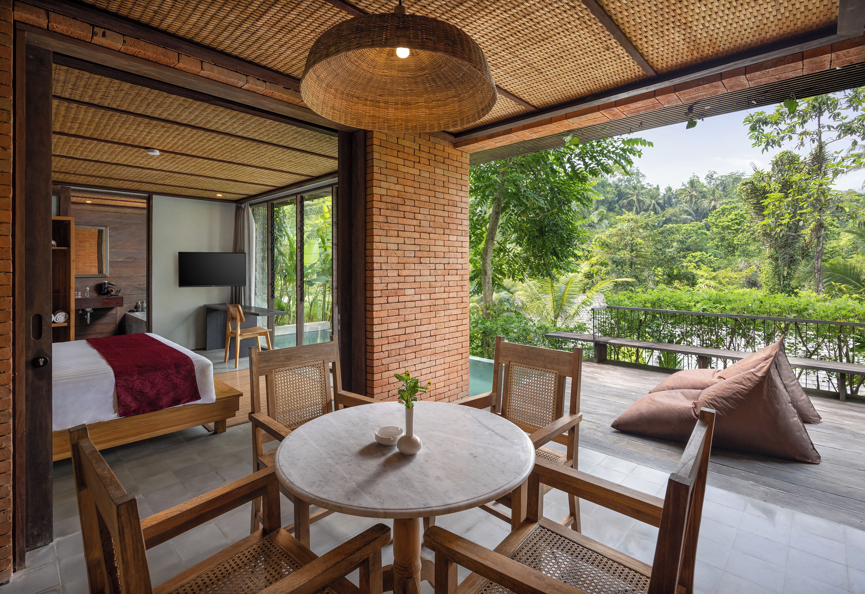 A room with a bed, a TV, a table with chairs, and a view of greenery outside.