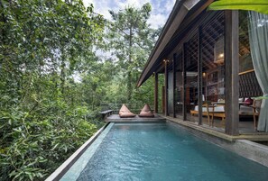 A pool with seating, surrounded by lush greenery and a modern building with large windows. - Hideaway Villas Bali – Ubud by Kanaan Hospitality (Ubud)