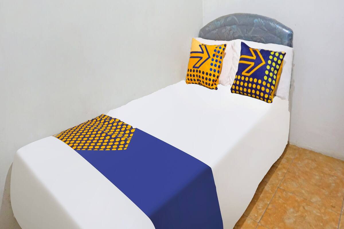 A single bed with a white mattress, a blue blanket, and two pillows with yellow and blue patterns.