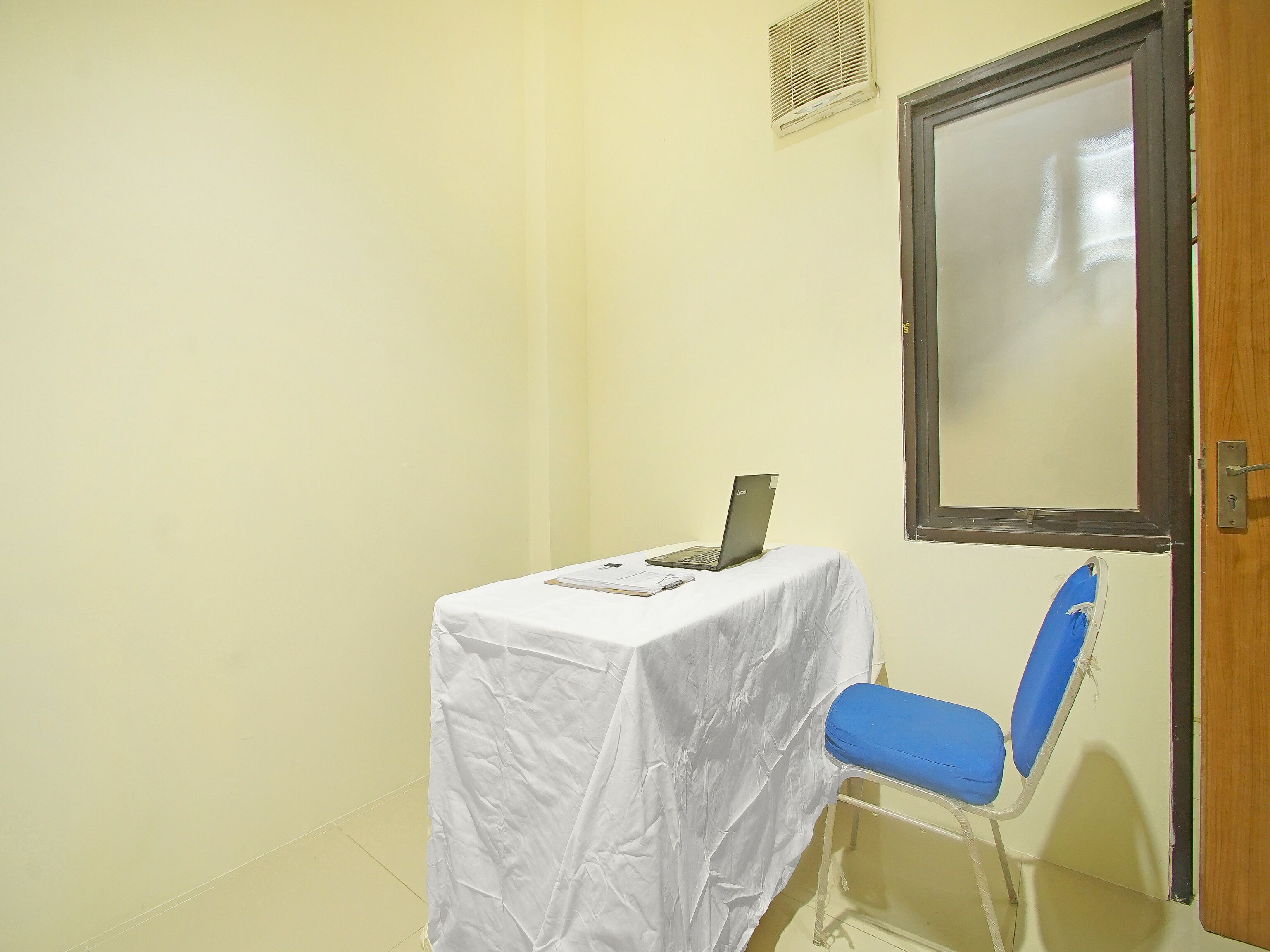 A small room with a table covered by a white cloth, a laptop, and a blue chair.