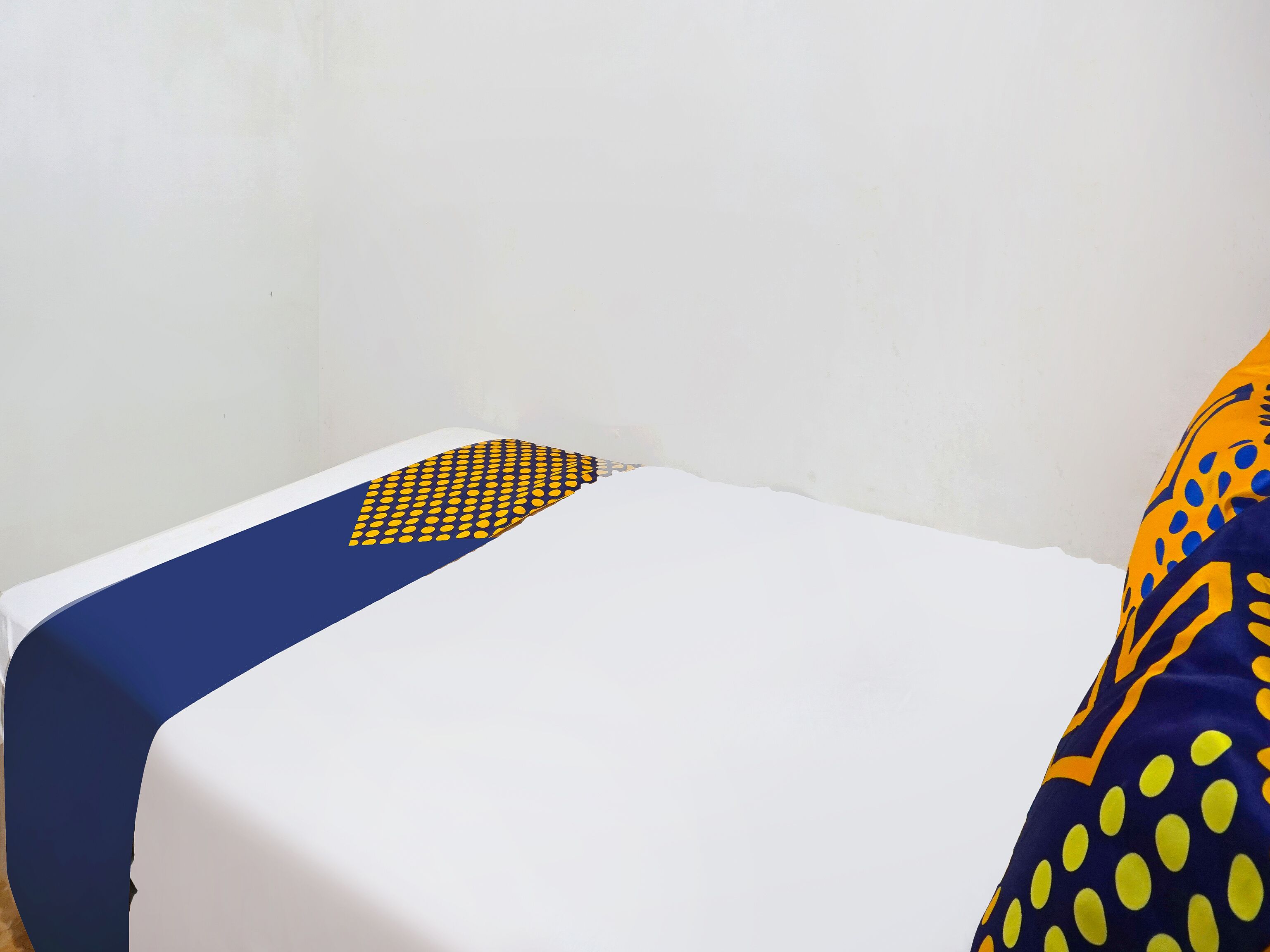 Una cama con sábana blanca y almohada de diseño azul y amarillo.