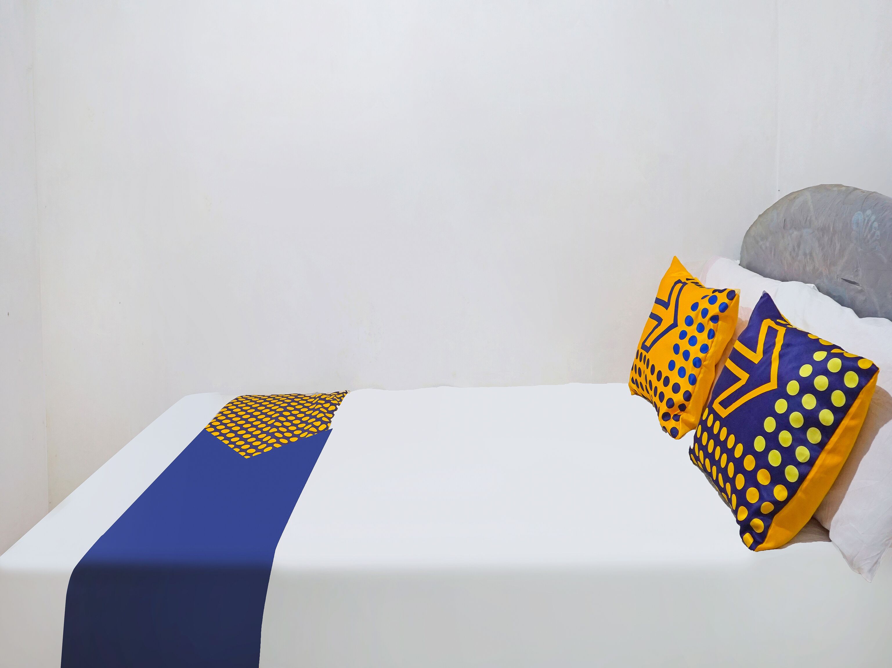 A bed with a white mattress, a blue and yellow bedspread, and two decorative pillows with yellow and blue patterns.