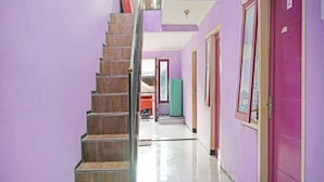 A hallway with a wooden staircase, purple walls, and a tiled floor. - OYO 91401 Almeera (Malang)