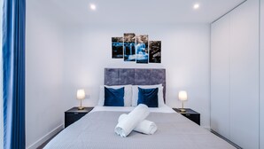 Moderni hotellihuone, jossa on suuri sänky, kaksi yöpöytää, sängynpääty ja seinälle kiinnitetty taideteos.