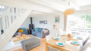 Een moderne woonkamer met een trap, een eethoek met een tafel gedekt voor twee personen, en een groot raam met uitzicht.