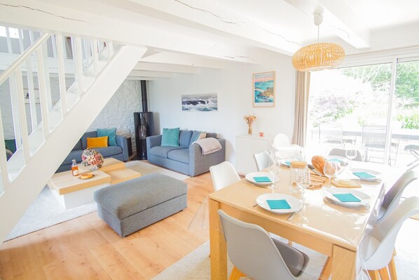 A modern living room with a staircase, a dining area with a table set for two, and a large window with a view.