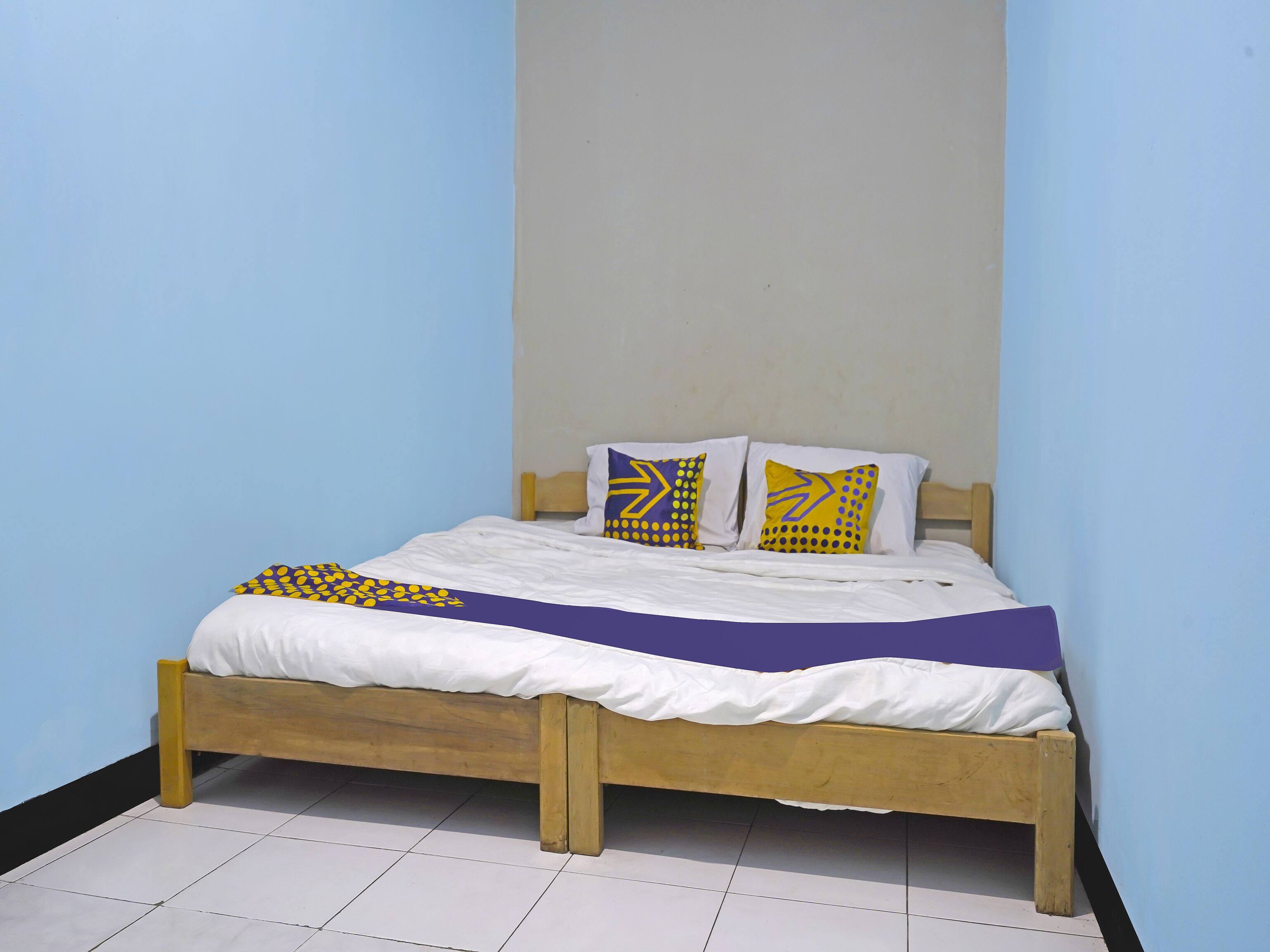 A single bed with a wooden frame, white bedding, and patterned pillows against a blue wall.