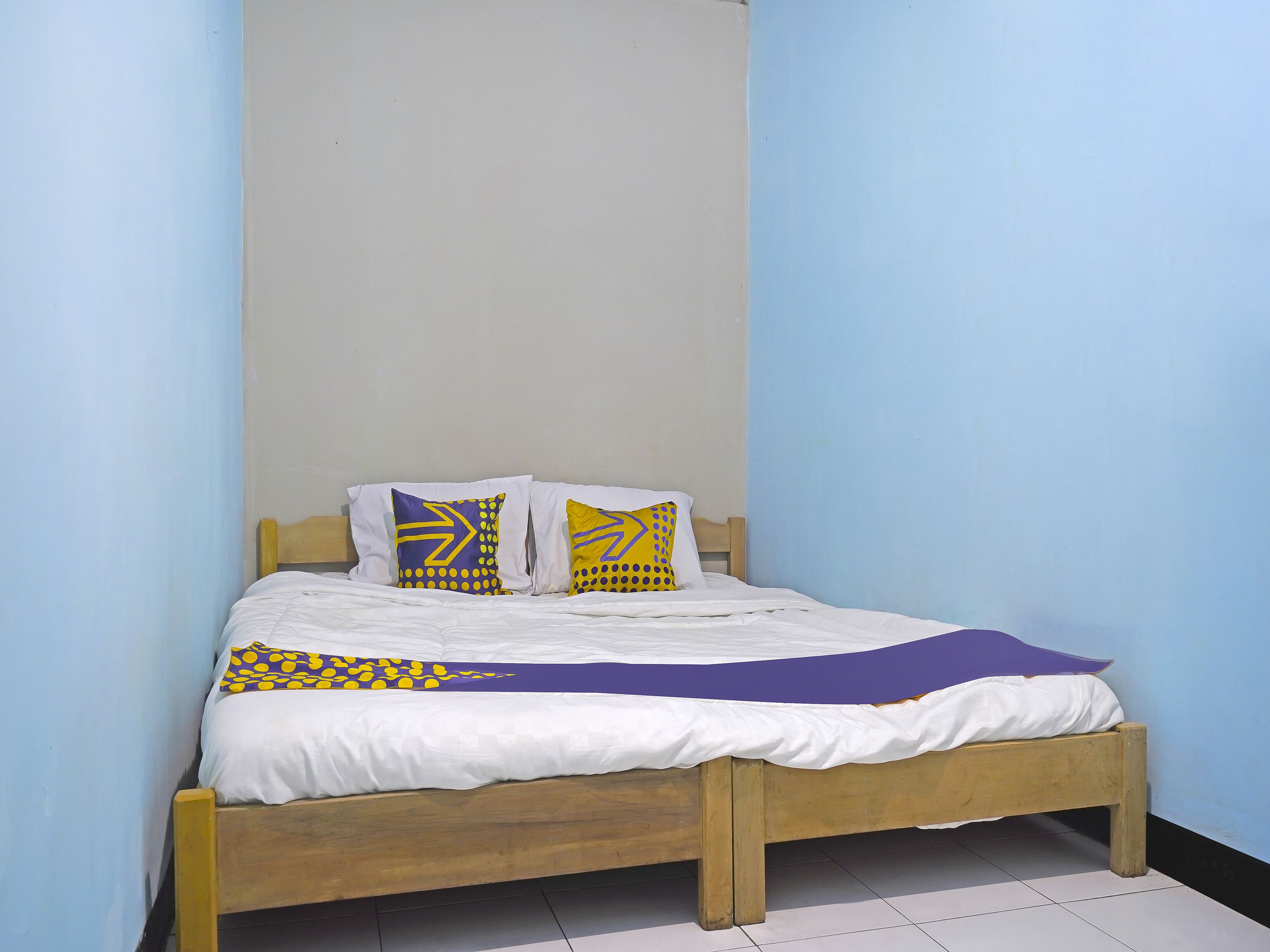 A single bed with a wooden frame, white bedding, and two decorative pillows with geometric patterns.