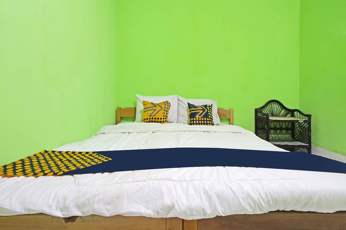 Ein Bett mit weißer Bettwäsche, zwei Kissen mit geometrischen Mustern, eine blaue und gelbe Decke sowie ein Holzkopfbrett.