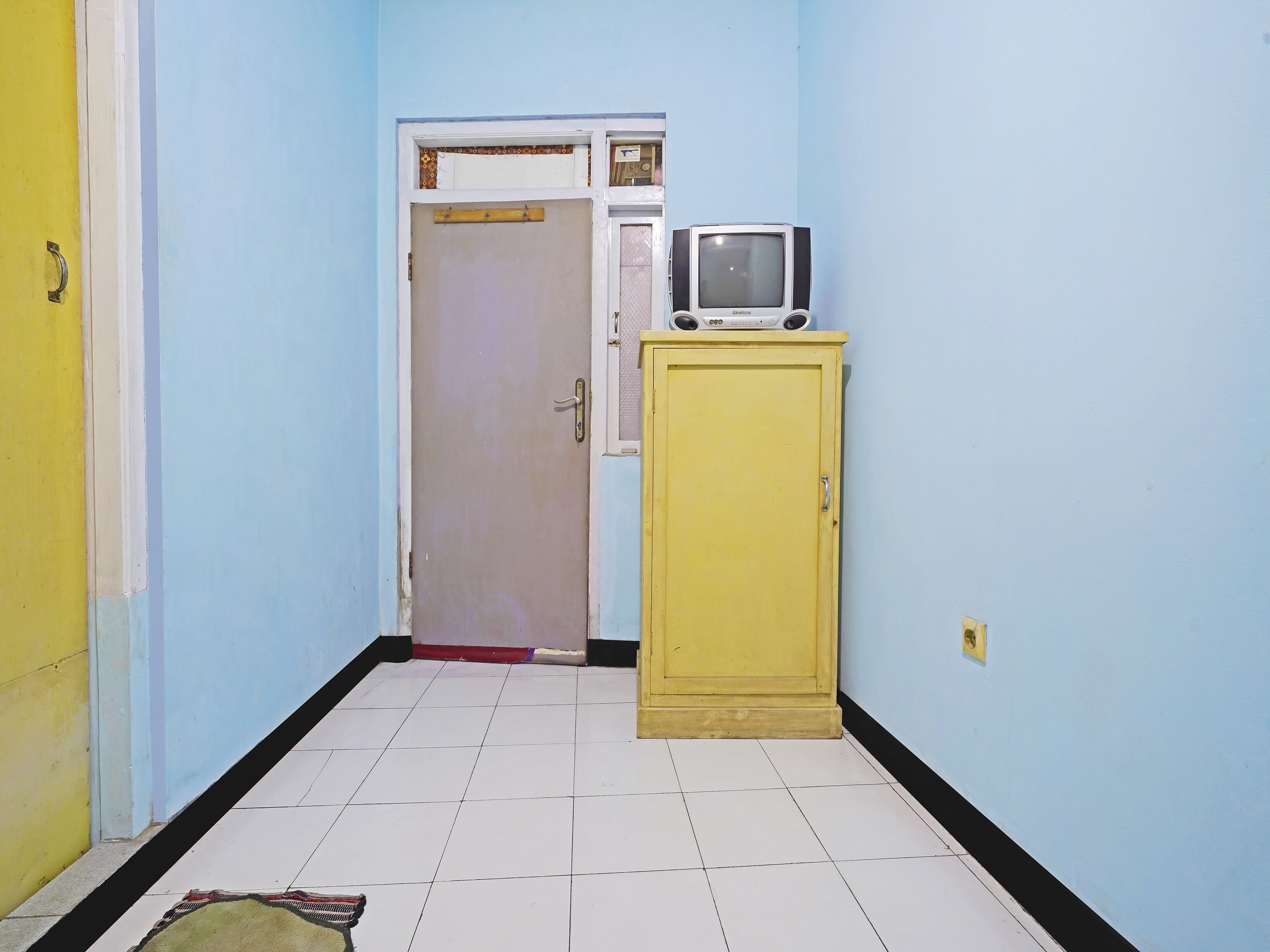 Um corredor com um armário amarelo, uma porta fechada e chão de azulejos.